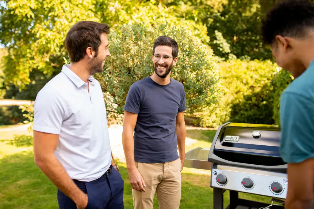 Amigos conversando cerca de una barbacoa en el jardín.