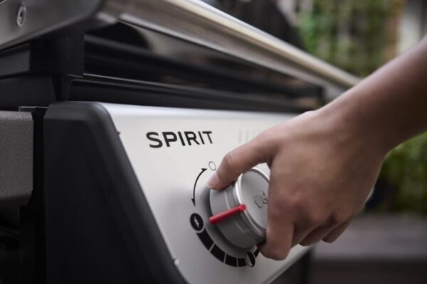 Mano ajustando control de barbacoa Spirit gris.