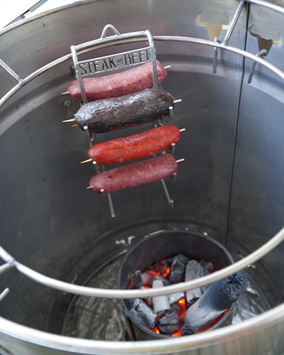 Salchichas colgando sobre brasas en parrilla metálica.