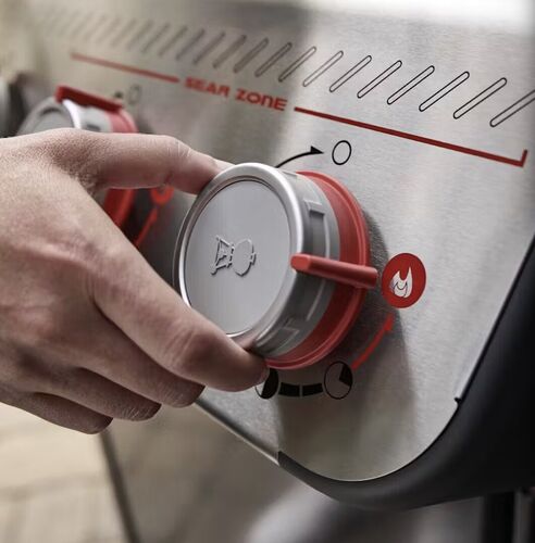 Mano ajustando perilla en parrilla de gas.