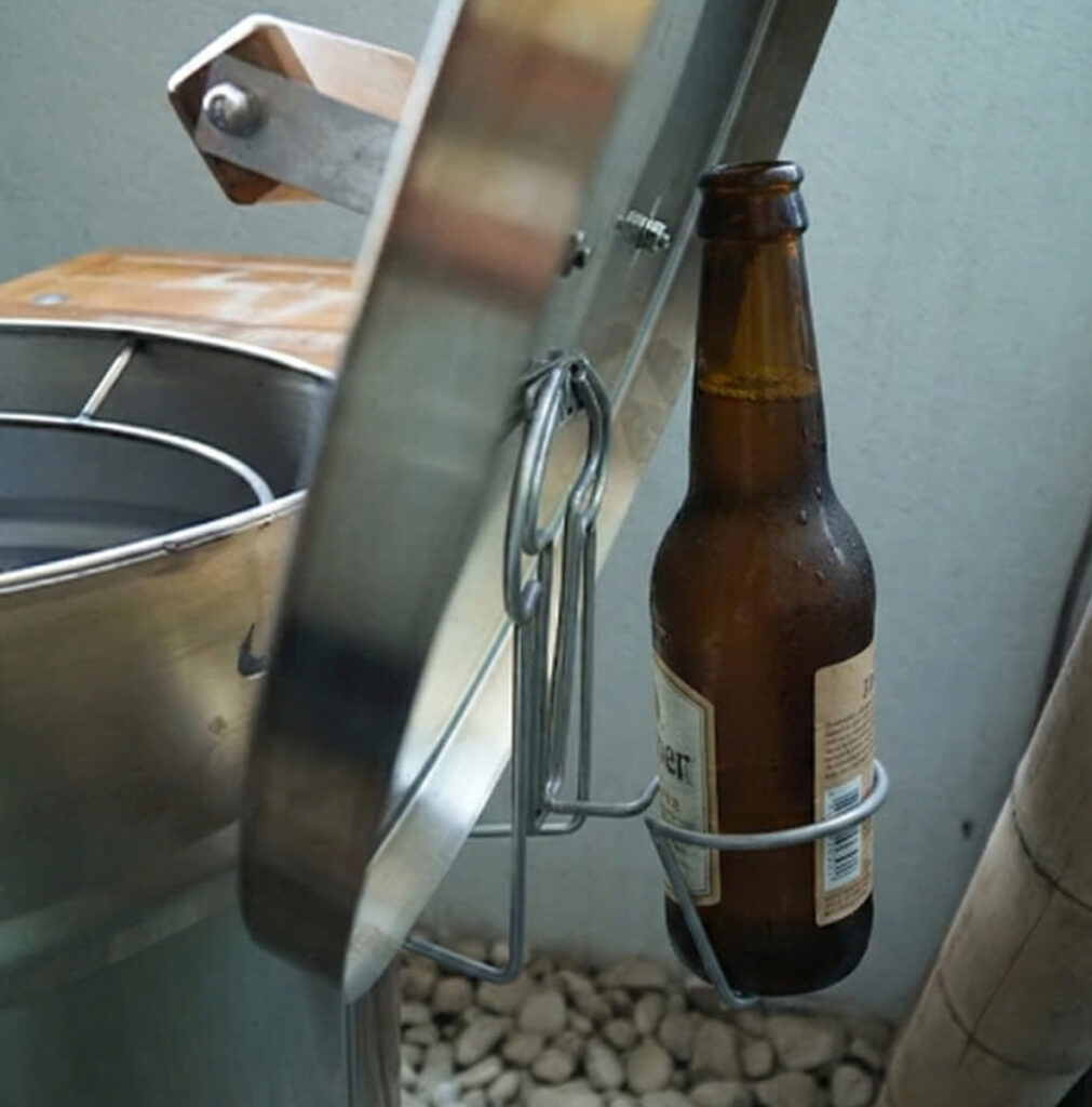 Botella de cerveza en soporte metálico junto a barbacoa